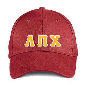 May include: A maroon baseball cap with the Greek letters ΛΠΧ in a gold color with a white outline. The cap has a curved brim and a button on top.