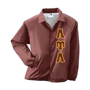 May include: A maroon coach jacket with a button-up front, collar, and two front pockets. The jacket features the Greek letters Lambda, Mu, and Lambda in a gold color with a brown outline on the front.