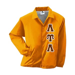 May include: Mustard yellow jacket with a button-up front, collared neckline, and two front pockets. The jacket features the Greek letters Lambda, Tau, and Alpha in brown with a white outline. The jacket is made of a smooth, lightweight material.
