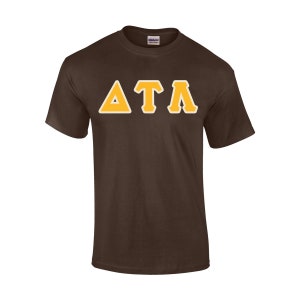 May include: A brown t-shirt with the Greek letters Delta, Tau, and Alpha in gold with a white outline. The shirt is made of a soft material and has a crew neck.