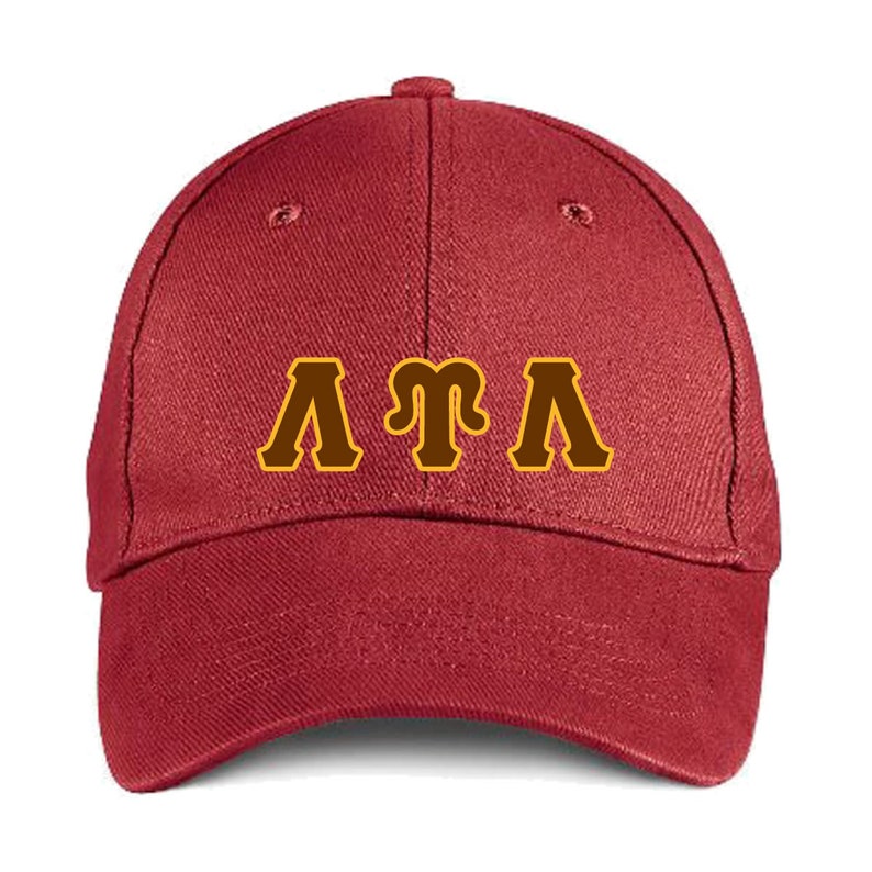 May include: A maroon baseball cap featuring the letters "ATA" in brown with a gold outline. The cap has a curved peak and a button on top. The hat is made of a soft fabric.