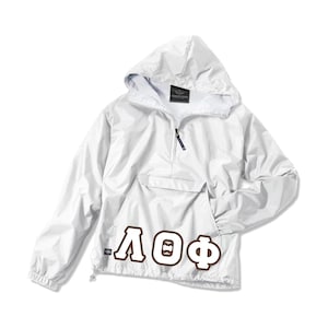 May include: White hooded anorak jacket with a front pocket and a half-zip closure. The jacket features brown Greek letters on the front. The jacket has a drawstring at the bottom hem and the brand name "CHARLES RIVER" is visible on the inside of the hood.