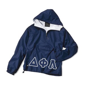 May include: Navy blue hooded anorak jacket with a white interior lining. The jacket features a front pocket, a half-zip closure, and white Greek letters. The jacket has a drawstring at the hem and elastic cuffs.