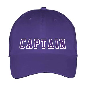 May include: A purple baseball cap with the word "CAPTAIN" in white block letters. The hat has a curved brim and a button on top. The text is outlined in white.