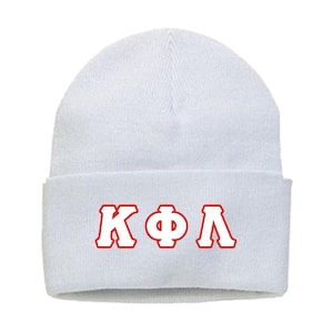 May include: A white beanie with a folded brim. The beanie features the Greek letters K, Φ, and Λ in red, outlined in white, centered on the folded brim. The hat is made of a soft, knitted material.