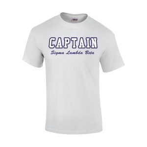 May include: White crew neck t-shirt with the word "CAPTAIN" in a navy blue outlined font, and the text "Sigma Lambda Beta" below it. The shirt is made of a soft, comfortable material.