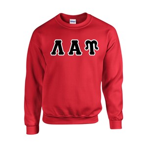 May include: A red crewneck sweatshirt with the letters "AAT" in black with a white outline across the chest. The sweatshirt is a solid red color and has a ribbed neckline, cuffs, and hem.