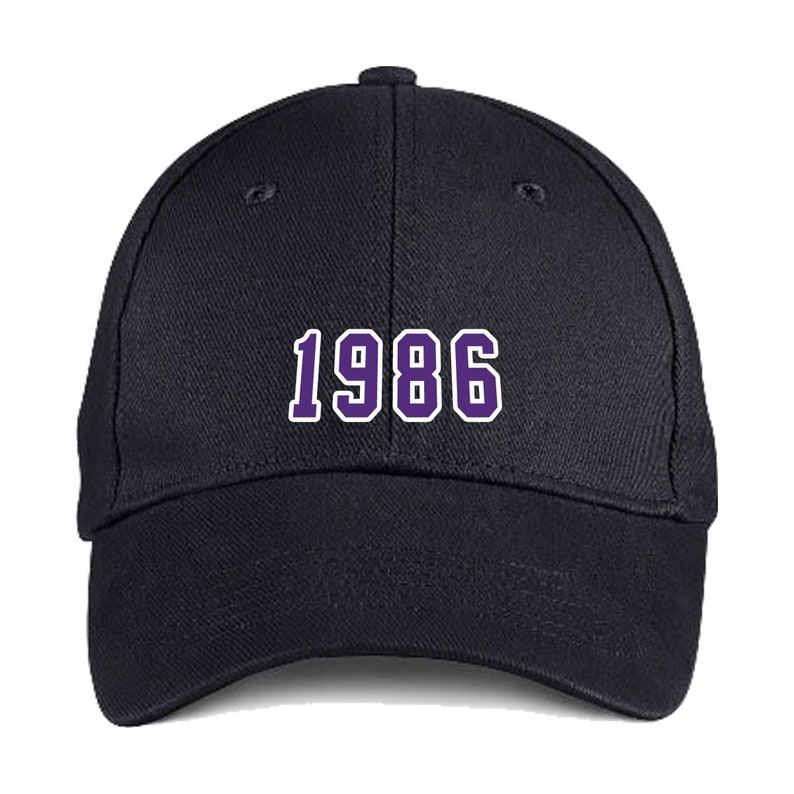 Puede incluir: Una gorra de b&eacute;isbol negra con el n&uacute;mero "1986" bordado en morado en la parte delantera.