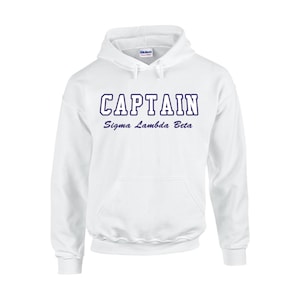 May include: White hooded sweatshirt with the word "CAPTAIN" in navy blue block letters above "Sigma Lambda Beta" in a script font. The sweatshirt has a front pocket and a drawstring hood.