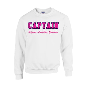 May include: White sweatshirt with the text "CAPTAIN" in blue and pink lettering. Below the text is "Sigma Lambda Gamma" in pink lettering.