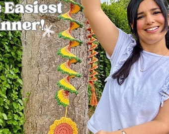 Könnte beinhalten: Ein gehäkelter Windspinner in Form einer Sonnenblume, mit gelben, orangefarbenen und grünen Farben. Der Text "Crochet the Easiest Wind Spinner!" ist sichtbar. Der Spinner hängt an einem Baum.