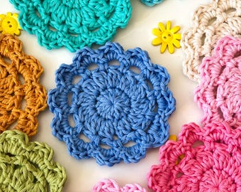 May include: A collection of colorful, handmade crochet coasters in shades of teal, blue, pink, yellow, green, and beige. The coasters have a circular, floral design and are made of soft yarn. The image is taken from a top-down perspective.