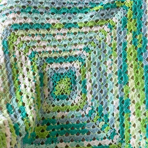 Peut inclure: Une couverture au crochet avec un motif carré dans des tons de vert, bleu et blanc.