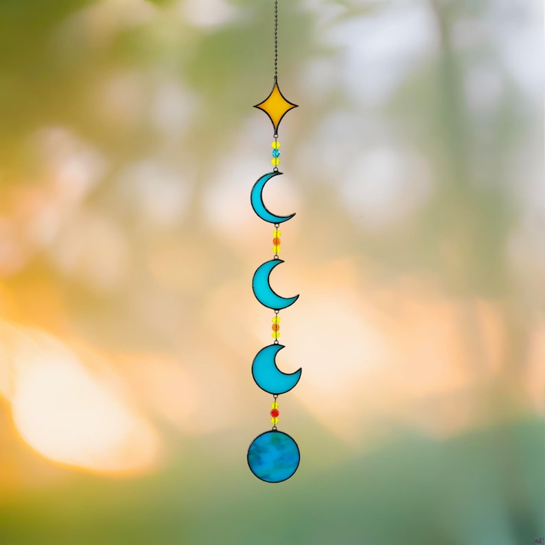 Op de afbeelding: Een decoratieve hanger met een gele ster, drie blauwe halve manen en een blauwe bol, verbonden door een ketting en kleurrijke kralen. Dit hemelse kunstwerk is ontworpen voor binnen of buiten.