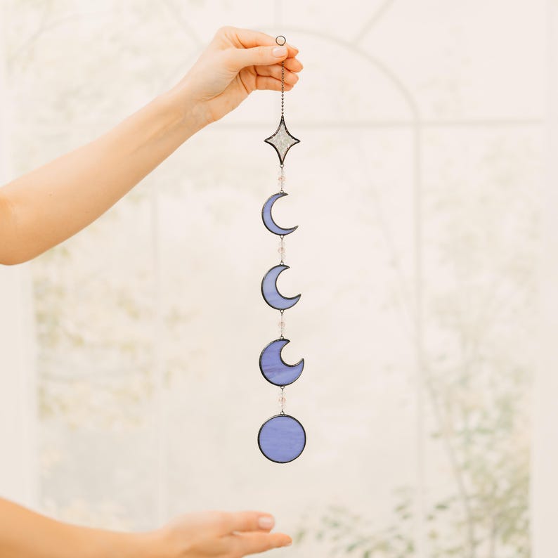 Op de afbeelding: Decoratieve hanger met maanfasen. Het ontwerp toont een ster, drie halve manen en een volle maan in blauwtinten. De fasen zijn verbonden door een ketting.