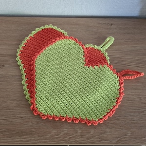Könnte beinhalten: Ein grün-oranger, gehäkelter Topflappen in Herzform mit einem gewellten Rand.