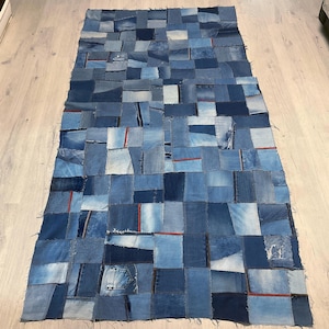 Peut inclure: Un tapis rectangulaire en patchwork de denim composé de carrés de tissu de jean de différentes nuances de bleu. Certains carrés ont des coutures rouges. Un article de décoration intérieure unique et fait à la main.