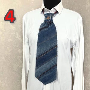 May include: A necktie crafted from strips of blue denim fabric with frayed edges, featuring a central metal button at the knot. The tie is worn over a crisp white long-sleeved button-down shirt. The number 4 is displayed in red in the upper left.