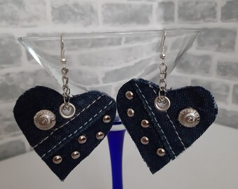 May include: A pair of denim heart-shaped earrings with silver studs and metal accents. The earrings are hanging from silver chains.