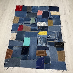 May include: A patchwork quilt made from denim fabric in various shades of blue, brown, and green. The quilt is made up of many different sized squares and rectangles, and the edges are frayed.