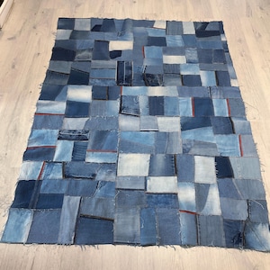 May include: A rectangular denim patchwork rug composed of various shades of blue denim squares. Some squares have red stitching. The rug is made from recycled denim and is suitable for a living room or bedroom.