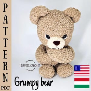 Puede incluir: Un oso de ganchillo marrón con una expresión gruñona, ojos negros y un hocico blanco. Los brazos del oso están cruzados y el texto "Grumpy bear" está debajo. La palabra "PATTERN" está escrita verticalmente en el lado izquierdo de la imagen. La imagen también incluye la bandera estadounidense.