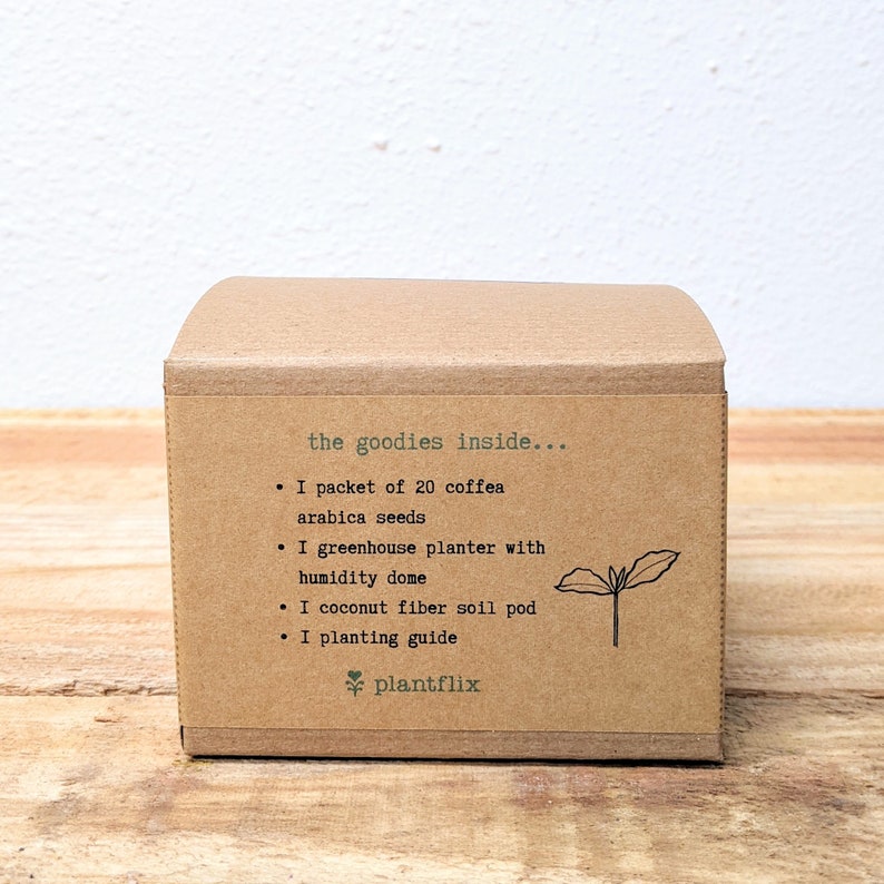 K&ouml;nnte beinhalten: Eine braune Pappschachtel mit dem Text "the goodies inside..." mit folgendem Inhalt: 20 Coffea Arabica-Samen, ein Gew&auml;chshaus-Pflanzgef&auml;&szlig; mit Feuchtigkeitskuppel, ein Kokosfaser-Erdballen und eine Pflanzanleitung. Das Plantflix-Logo befindet sich unten.