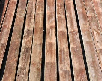 May include: A collection of weathered, reddish-brown wooden planks. The planks are arranged parallel to each other, with visible grain and knots, suggesting a rustic or reclaimed aesthetic. The wood shows signs of age and exposure.