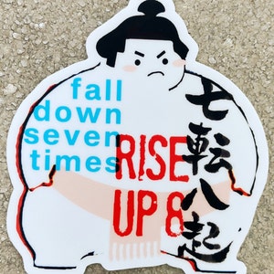 May include: White sticker with a cartoon sumo wrestler with the text "fall down seven times RISE UP 8" in red and blue. The wrestler has black hair and a serious expression. The background is white with black Japanese characters.