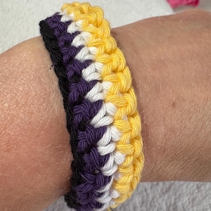 May include: A crocheted bracelet with yellow, white, purple and black stripes.