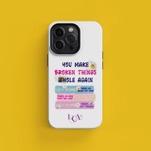 May include: White phone case with a floral design and the text "YOU MAKE BROKEN THINGS WHOLE AGAIN". The text "LUCY SCORE" appears three times with different text below each.
