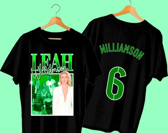 May include: Black t-shirt with a green graphic print of a woman's face and the text "LEAH Williamson" and a group of people. The back of the shirt has the text "WILLIAMSON" and the number "6" in green.