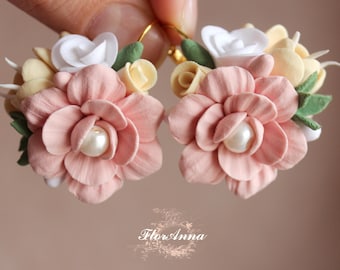 May include: A pair of pink and white floral earrings with pearl accents. The earrings are made of polymer clay and have a delicate, feminine design.