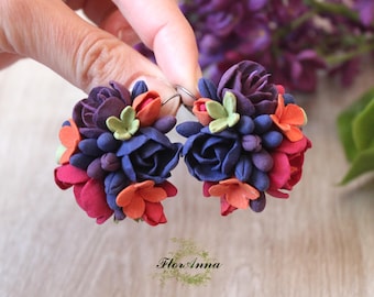 Op de afbeelding: Een paar bloemenoorbellen met een cluster van blauwe, paarse, rode en oranje bloemen. De oorbellen zijn gemaakt van polymer clay en hebben een zilveren haak.