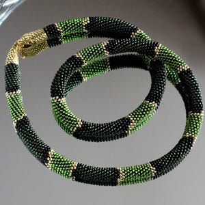 May include: A green and black beaded snake necklace with a gold snake head charm. The necklace is made of small, round beads and is coiled in a circle.