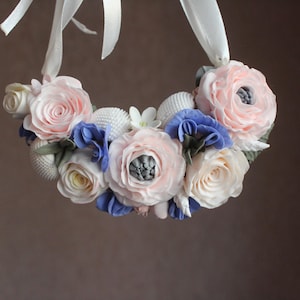 May include: A floral wreath with pastel pink, blue, and cream-coloured flowers. White ribbons are attached at the top. This decorative wreath is suitable for weddings or other celebrations.
