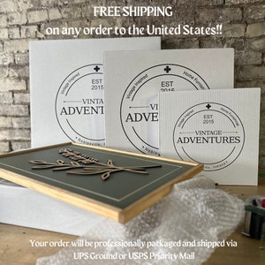 May include: Three white cardboard boxes with black text and logos. The boxes are stacked on top of each other. The top box has the text "Vintage Inspired" and "EST 2015" and the logo "Vintage Adventures". The middle box has the text "Vintage Inspired" and "EST 2015" and the logo "Vintage Adventures". The bottom box has the text "Home Furnishings" and "EST 2015" and the logo "Vintage Adventures".