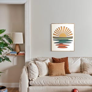 May include: A framed print of a sunset over a body of water. The sun is depicted as a yellow circle with orange rays emanating from it. The water is represented by a series of blue, green, and orange stripes.