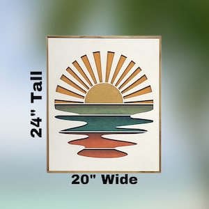 May include: A wooden framed wall art piece with a sunset over a lake design. The sun is yellow with orange rays and the lake is green, blue, and orange. The piece measures 20 inches wide and 24 inches tall.