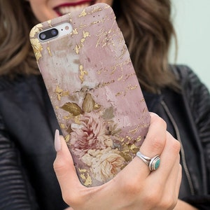 May include: A pink and gold iPhone case with a floral design and handwritten script. The case has a textured, distressed look.
