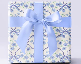 May include: A gift box wrapped in white paper with a blue floral pattern and a light blue satin ribbon tied in a bow.