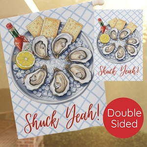 May include: Double-sided garden flag featuring a plate of oysters on ice, crackers, lemon, and hot sauce. The flag has a blue and white checkered background and the words "Shuck Yeah!" in red script.