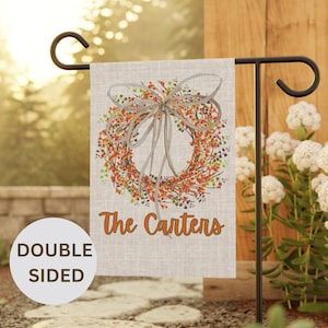 May include: A double-sided garden flag with a wreath design featuring orange and red flowers and a gray bow. The text "The Carters" is printed below the wreath.