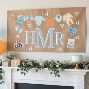 Può includere: Un banner marrone con illustrazioni a tema baby e le lettere HMR in azzurro. Il banner include immagini di vestiti per bambini, un bavaglino, un orsacchiotto e la frase "it's a boy!". Sono visibili anche una torta e dei palloncini.