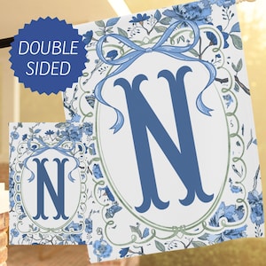 May include: Double-sided garden flag featuring a large blue letter "N" within an oval frame, adorned with a blue ribbon and floral pattern on a white background. The flag has a matching smaller version.