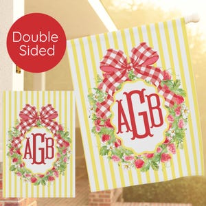 May include: A double-sided garden flag with a yellow and white striped design. It features a red gingham bow, a strawberry wreath, and a red monogram with the letters AGB. The flag is suitable for outdoor use and is designed to be displayed.