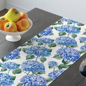 Pode incluir: Um corredor de mesa branco com um padrão floral azul e verde. O padrão apresenta hortênsias azuis com folhas verdes.