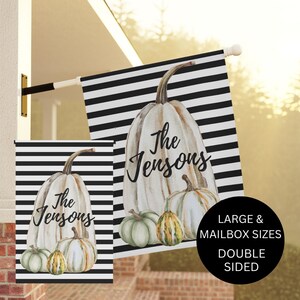 May include: A black and white striped garden flag with a watercolor pumpkin design. The pumpkin is white with brown accents and has the text "The Jensons" written on it. There are three smaller pumpkins in front of the large pumpkin. The flag is available in large and mailbox sizes and is double-sided.