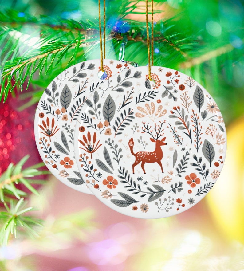 May include: White ceramic Christmas ornament with a red deer and floral pattern. The ornament is round and has a gold string for hanging.