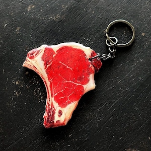 Puede incluir: Un llavero con forma de bistec rojo y blanco con un anillo de metal plateado.